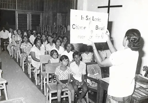 A teacher holding up a sign for children seated in a church hall