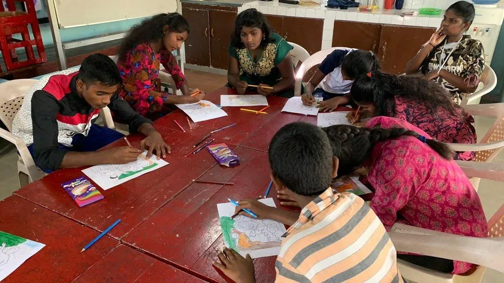 Teenagers drawing and colouring around a classroom table
