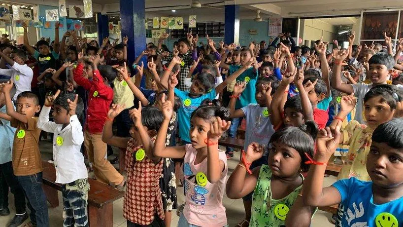 A hall full of excited children with their hands in the air at an outreach program